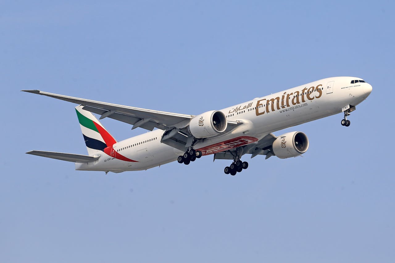 A striking image of an Emirates Boeing 777 soaring through a clear blue sky, wings extended.