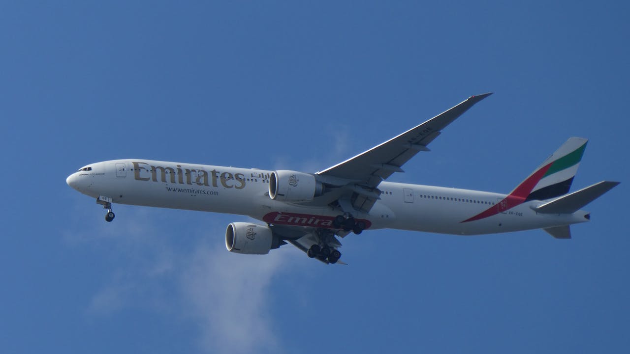 A sleek Emirates airplane flying against a backdrop of clear blue sky, showcasing modern aviation.