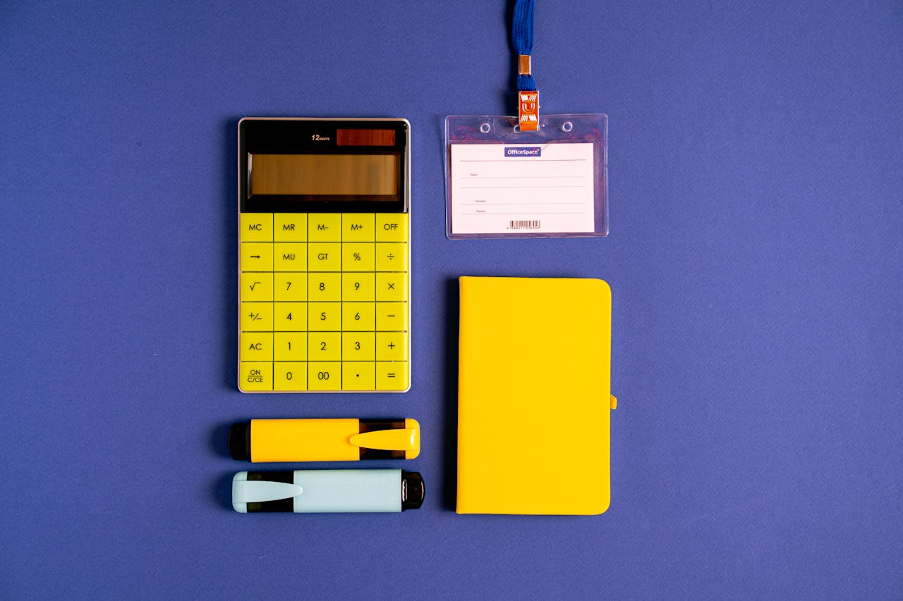 Bright yellow calculator, notebook, and markers on a blue surface for office or school use.